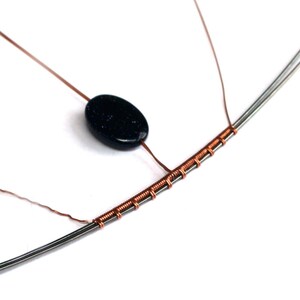 May include: A black oval-shaped gemstone bead is strung on a copper wire wrapped around a silver wire. The wire is wrapped in a series of coils.