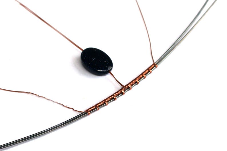 May include: A black oval-shaped gemstone bead is strung on a copper wire wrapped around a silver wire. The wire is wrapped in a series of coils.