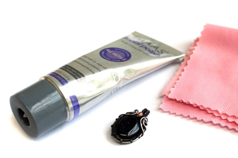 May include: A silver tube of jewelry polish with the text "IAS Jewel Polish" and "All Metals" on the label. A pink polishing cloth and a black gemstone pendant with silver wire wrapping are also pictured.
