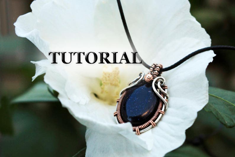 May include: Wire-wrapped pendant necklace featuring a dark blue gemstone. The pendant is crafted with silver and copper wire, creating an intricate design.  The word TUTORIAL is prominently displayed. The necklace is shown resting on a white flower. The gemstone has a speckled texture.