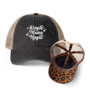 May include: A black trucker hat with the text "Single Mama Magic" in white script. The hat has a tan mesh back and a leopard print pattern on the underside of the brim. A stylish accessory.