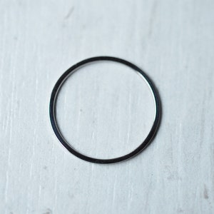 Pu&ograve; includere: Un anello di metallo color argento, posto piatto su una superficie di legno bianco.