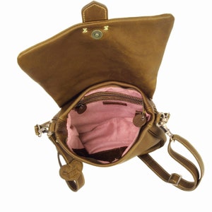 May include: A brown leather crossbody bag with a flap closure and a heart-shaped charm. The bag has a pink fabric lining and a zippered pocket inside.