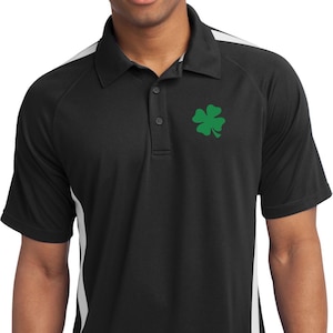 Puede incluir: Polo negro con rayas laterales blancas y un logotipo de trébol verde en el pecho. La camisa tiene cuello y tapeta de tres botones. Las mangas son cortas y la tela parece ser un material que absorbe la humedad.