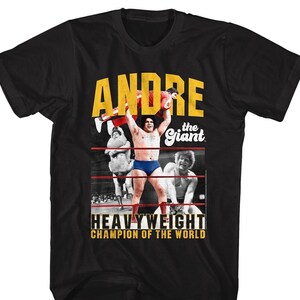 May include: Black t-shirt featuring a yellow graphic of Andre the Giant, a professional wrestler, holding another wrestler above his head. The graphic includes the text "Andre the Giant" and "Heavyweight Champion of the World".