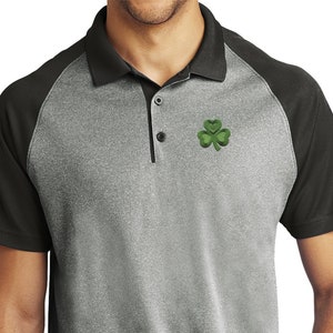 May include: A gray and black short-sleeved polo shirt with a green shamrock embroidered on the left chest.