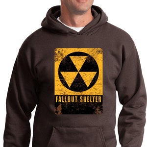 May include: A brown hooded sweatshirt with a yellow and black vintage fallout shelter sign printed on the front. The sign features a black triangle symbol with three points.
