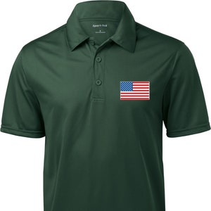 May include: A forest green short-sleeved polo shirt with a small American flag embroidered on the left chest. The shirt has a button-down collar and a three-button placket.