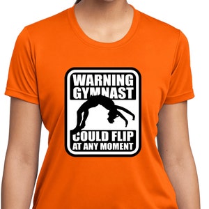 Pode incluir: Camiseta esportiva laranja para mulher com um gráfico em preto e branco de uma ginasta com o texto "Warning Gymnast Could Flip At Any Moment".