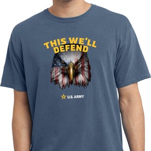 Puede incluir: Una camiseta azul con un aspecto desgastado que presenta un águila calva con un diseño de bandera estadounidense. El texto "THIS WE'LL DEFEND" está por encima del águila y "U.S. ARMY" está por debajo del águila.