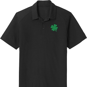 Puede incluir: Una camiseta polo negra con un trébol de cuatro hojas verde bordado en el lado derecho del pecho.