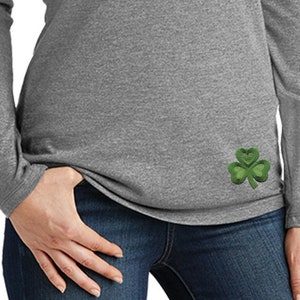 以下が含まれることがあります： 左側に緑色のクローバーが刺繍されたグレーの長袖フード付きシャツ