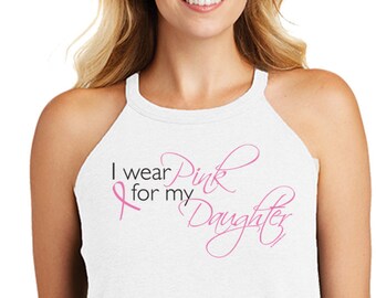 Puede incluir: Top blanco sin mangas con el texto "I wear Pink for my Daughter" en letras negras y rosas. El top presenta un lazo rosa, símbolo de la concienciación sobre el cáncer de mama. La mujer lleva vaqueros azul oscuro.