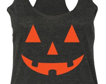 Może przedstawiać: Ciemnoszary tank top typu racerback z jaskrawopomarańczową grafiką przedstawiającą twarz dyni na przodzie. Wzór zawiera dwoje trójkątnych oczu, trójkątny nos oraz szeroki, wyszczerbiony uśmiech nadrukowany na środku części garderoby.