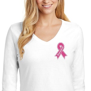 Peut inclure: T-shirt à manches longues blanche à col en V avec un ruban rose et le mot "Survivor" brodé sur la poitrine gauche.
