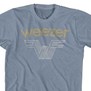 May include: A light blue t-shirt featuring the band name "weezer" in gold lettering above a stylized "W" logo in white and gold. The shirt is made of a soft material and has short sleeves.