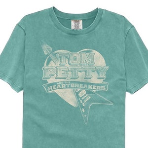 May include: A teal blue t-shirt with a vintage-style graphic of a heart with a guitar and the text "Tom Petty and the Heartbreakers".