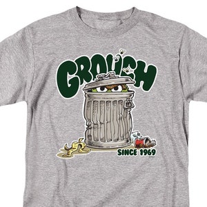 May include: A gray t-shirt with a green cartoon image of Oscar the Grouch from Sesame Street. The image shows Oscar inside a trash can with the text "Grouch" above him and "Since 1969" below him.