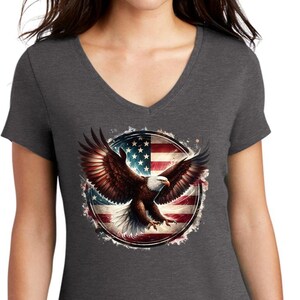 May include: A dark heather grey V-neck t-shirt with a graphic of a bald eagle flying in front of an American flag.