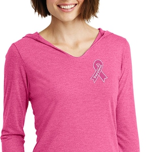 May include: Pink long-sleeved hooded shirt with a pink ribbon and the word "survivor" embroidered on the left chest.