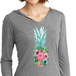 May include: A gray long-sleeved hooded shirt with a pineapple design. The pineapple is made of watercolor and has pink and blue flowers around it.