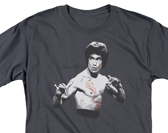 May include: A dark gray t-shirt featuring a black and white image of Bruce Lee with red markings on his chest. The text "Bruce Lee" is written in white above the image.