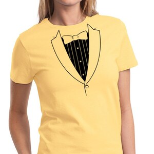 May include: A yellow t-shirt with a black tuxedo graphic printed on the front. The tuxedo has a bow tie and a button.