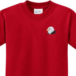 May include: Red short-sleeved t-shirt with an embroidered bald eagle on the left chest.