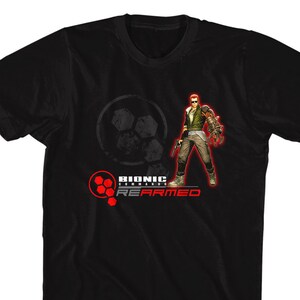 May include: Black t-shirt with a red and white logo that says "Bionic Commando Rearmed". The logo features a character with a robotic arm.