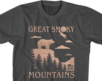 May include: A dark gray t-shirt with a brown bear silhouette standing on a cliff with trees and clouds. The text "GREAT SMOKY MOUNTAINS" is printed in brown on the shirt. The National Parks Conservation Association logo is also printed on the shirt.