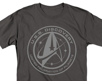 May include: A dark gray t-shirt with a gray and white graphic of the U.S.S. Discovery logo from Star Trek: Discovery. The logo features the text "U.S.S. Discovery" and "United Federation of Planets" around a stylized starfleet insignia.