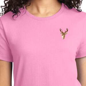 Può includere: Una t-shirt rosa da donna con un piccolo disegno di testa di cervo ricamato sul petto sinistro.