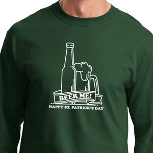 Peut inclure: Un t-shirt à manches longues vert avec un motif blanc d'une bouteille de bière et d'une chope avec le texte "Beer Me! Happy St. Patrick's Day".