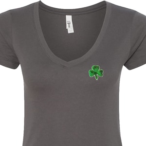 May include: Dark grey V-neck t-shirt with a green shamrock design on the left chest.
