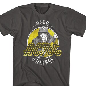May include: A dark gray t-shirt with a yellow circle graphic featuring a man playing a guitar. The graphic also includes the text "HIGH VOLTAGE" and the band name "AC/DC" in yellow letters.