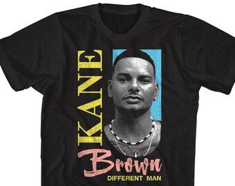 May include: Black t-shirt featuring a portrait of Kane Brown with the text "KANE" in yellow, "Brown" in pink, and "Different Man" in white. The portrait is set against a blue background. The shirt is a classic crew neck style.