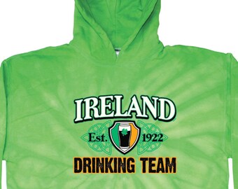 以下が含まれることがあります： 緑色のタイダイ染めのフード付きスウェットシャツ。白いプリントで「アイルランド Est. 1922 ドリンキングチーム」と書いてあり、クローバーとビールジョッキが盾の中に描かれている。