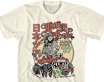 Può includere: Una t-shirt bianca con una grafica in stile vintage di un monster truck con una figura al volante. La grafica include il testo "Motley Crue" e "Japan Tour '87".