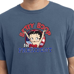 May include: A blue t-shirt with a vintage-style graphic of Betty Boop with the text "Betty Boop for President" in a red, white, and blue circle.