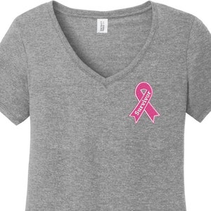 以下が含まれることがあります： VネックのヘザーグレーのTシャツに、ピンクのリボンと白い文字で「Survivor」と書かれている。
