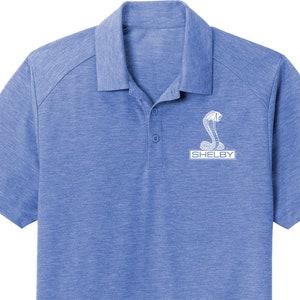 May include: A blue short-sleeved polo shirt with a white embroidered Shelby Cobra logo and the word "Shelby" underneath.