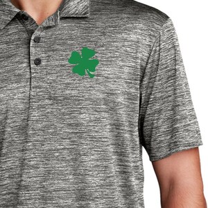 Puede incluir: Una camiseta polo de manga corta gris jaspeada con un trébol de cuatro hojas verde bordado en el pecho izquierdo.