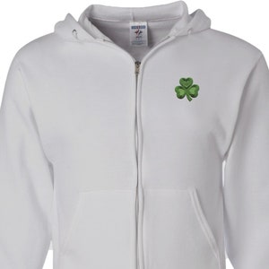 May include: A white zippered hoodie with a green shamrock embroidered on the left chest. The hoodie is made of a soft, comfortable fabric and has a relaxed fit.