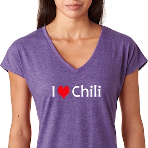 Puede incluir: Camiseta morada de cuello en V con un gráfico blanco que dice "Me encanta el chile" con un corazón rojo.