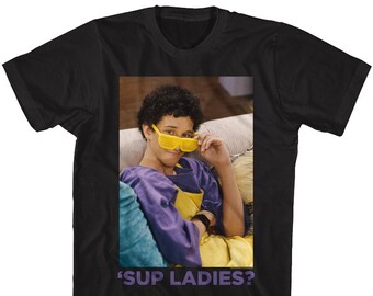 May include: A black t-shirt with a photo of a young man wearing yellow sunglasses and a purple shirt. The text "'Sup Ladies?" is printed on the shirt.