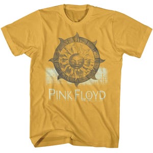 May include: A mustard yellow t-shirt with a vintage-style graphic of a sun with a face and the text "PINK FLOYD" printed on the front.