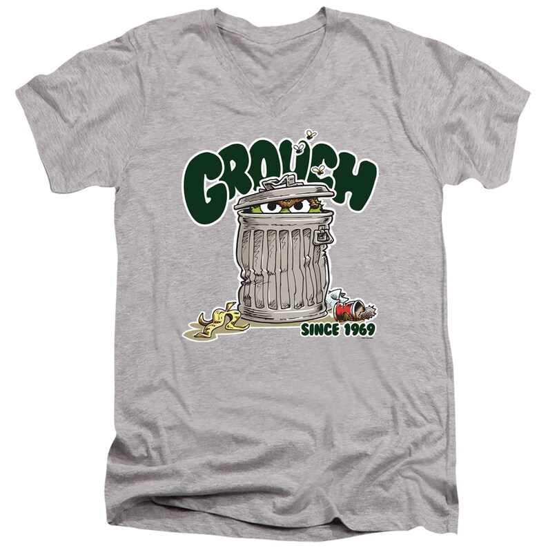 May include: A gray V-neck t-shirt with a green cartoon of Oscar the Grouch peeking out of a trash can. The text "Grouch" is above the trash can and "Since 1969" is below the trash can.