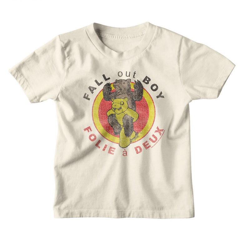May include: A white t-shirt with a vintage-style graphic of two bears in a red and yellow circle. The text "Fall Out Boy" is written around the circle, and the text "Folie a Deux" is written below the circle.