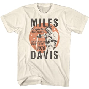 May include: A white t-shirt with a vintage-style graphic of Miles Davis playing a trumpet. The graphic includes the text "Miles Davis", "Schaefer Music Festival", "Central Park, NY", "Monday, July 6th", and "1970".