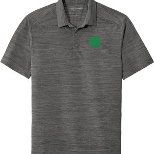 Puede incluir: Una camiseta polo de manga corta gris jaspeada con un trébol de cuatro hojas verde bordado en el pecho izquierdo.